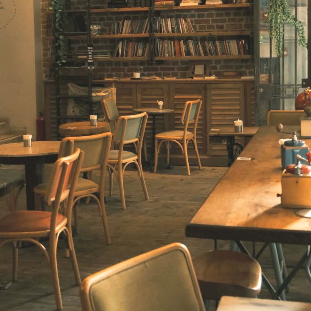 Interior del café con libreros de madera, mesas redondas y sillones